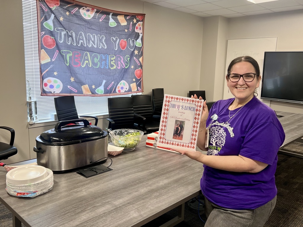 A person in a purple shirt holds a framed photo in a room with a table.