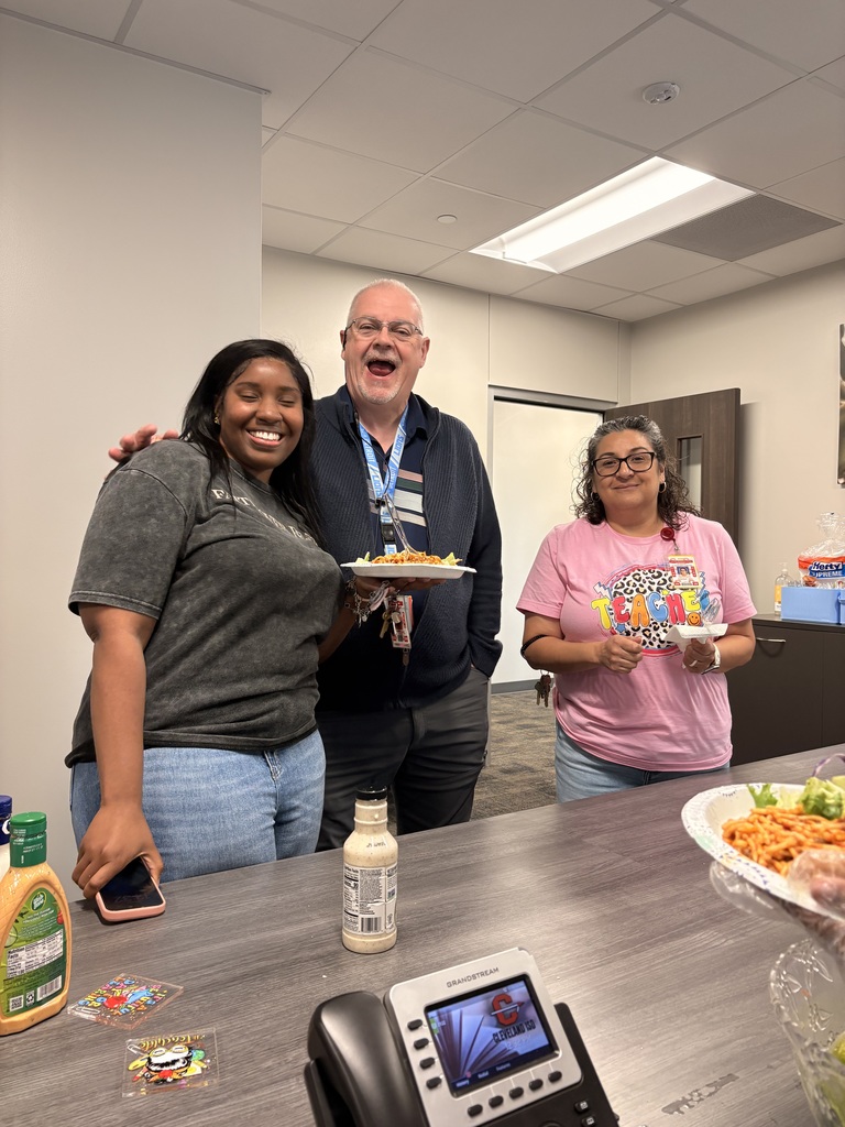 Three people stand near a table in a room with food, drinks, and a phone. A woman holds a plate.