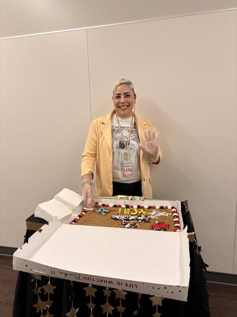 A woman wearing a yellow jacket and gloves stands beside a box containing a decorated cake.