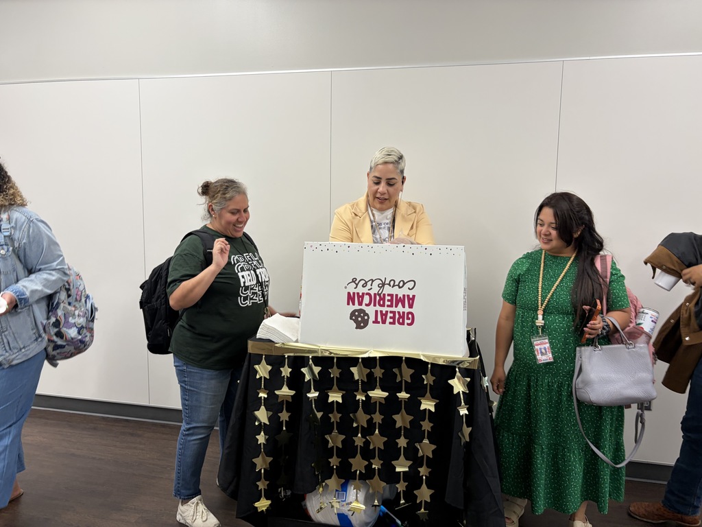 Four people stand around a table with a sign that reads "GRADUATE 2021". One person stands behind the table.