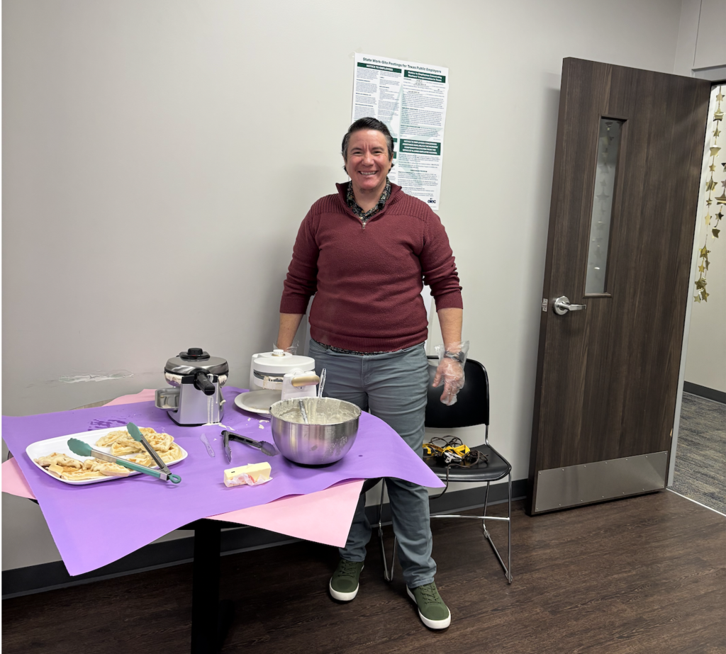 A person stands by a table with bowls, plates, and utensils. Behind them is a door and a bulletin board.