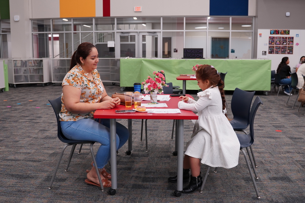 Woman and young girl sit at table, writing. Behind them, a green banner is visible.