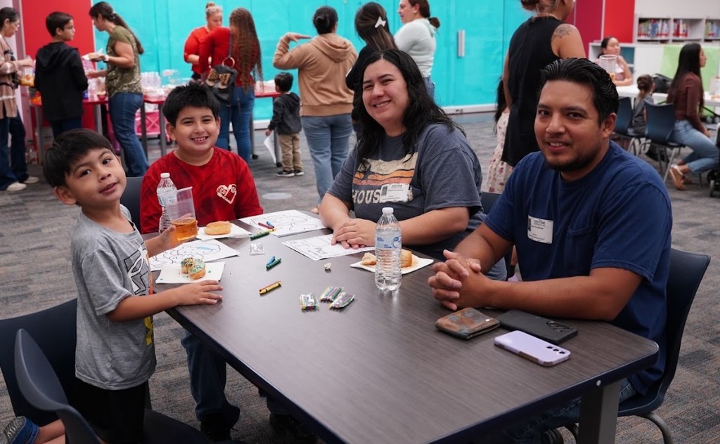A family sits at a table inside a library, with food and drink in front of them.
