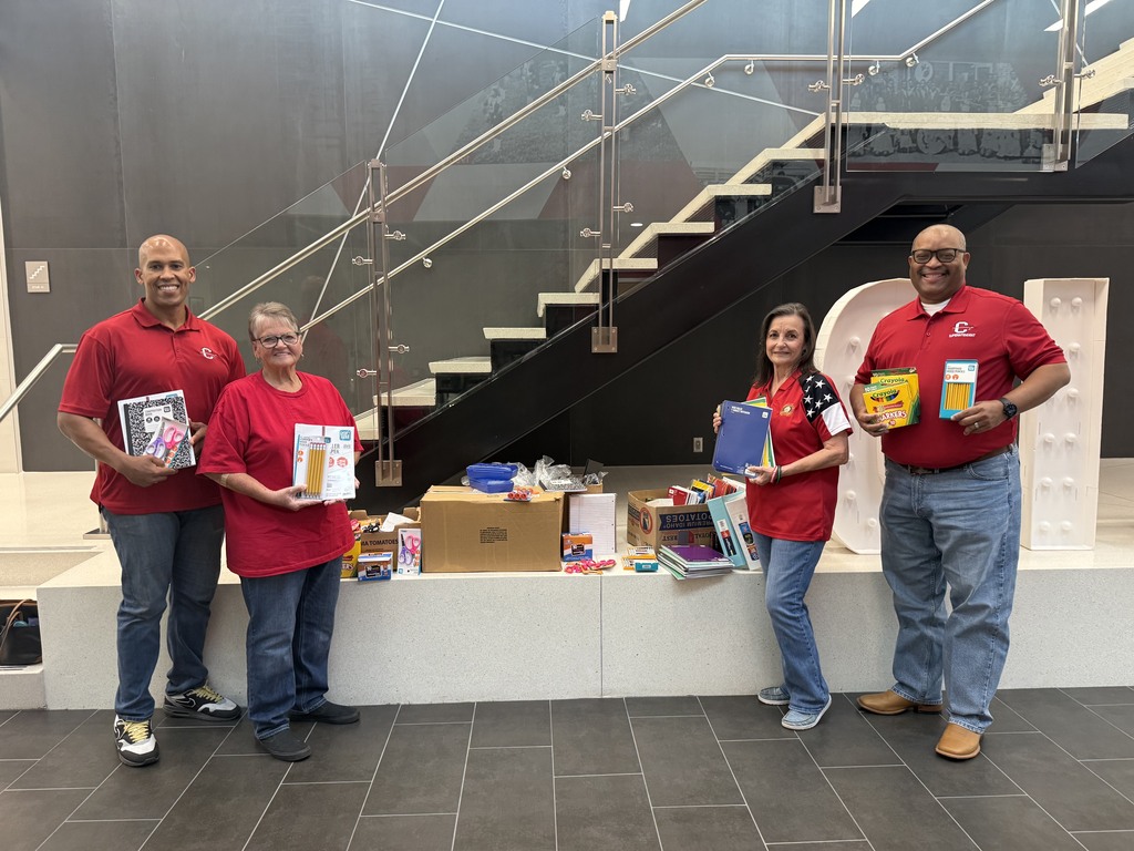 4 individuals standing holding school supplies smiling