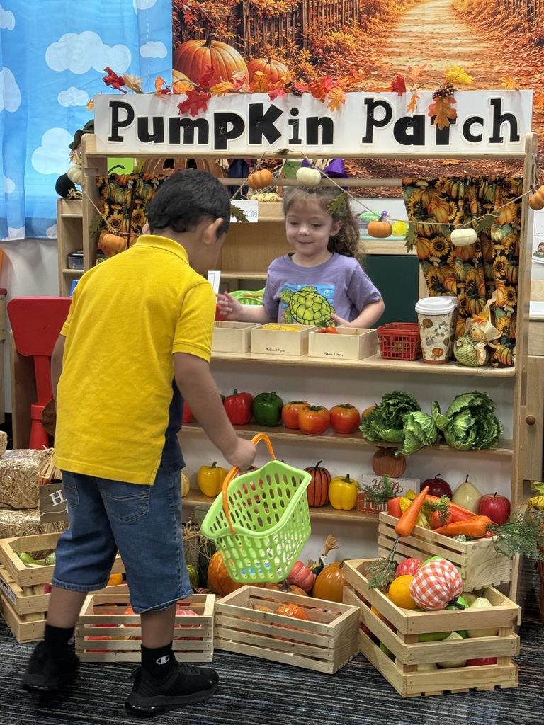 Child in yellow shirt holding basket in front of a wooden store with a pumpkin patch sign.