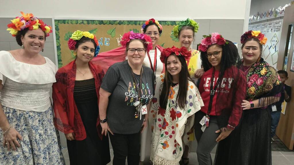 A group of women in traditional attire, wearing flower headdresses, standing together indoors.