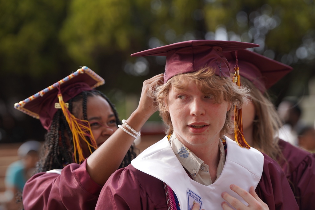 Seniors helping friend fix their cap before graduation