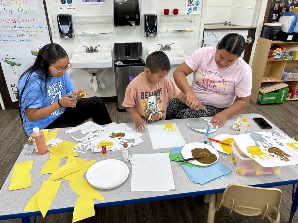 2 high school students helping a Head Start student with a handprint painting