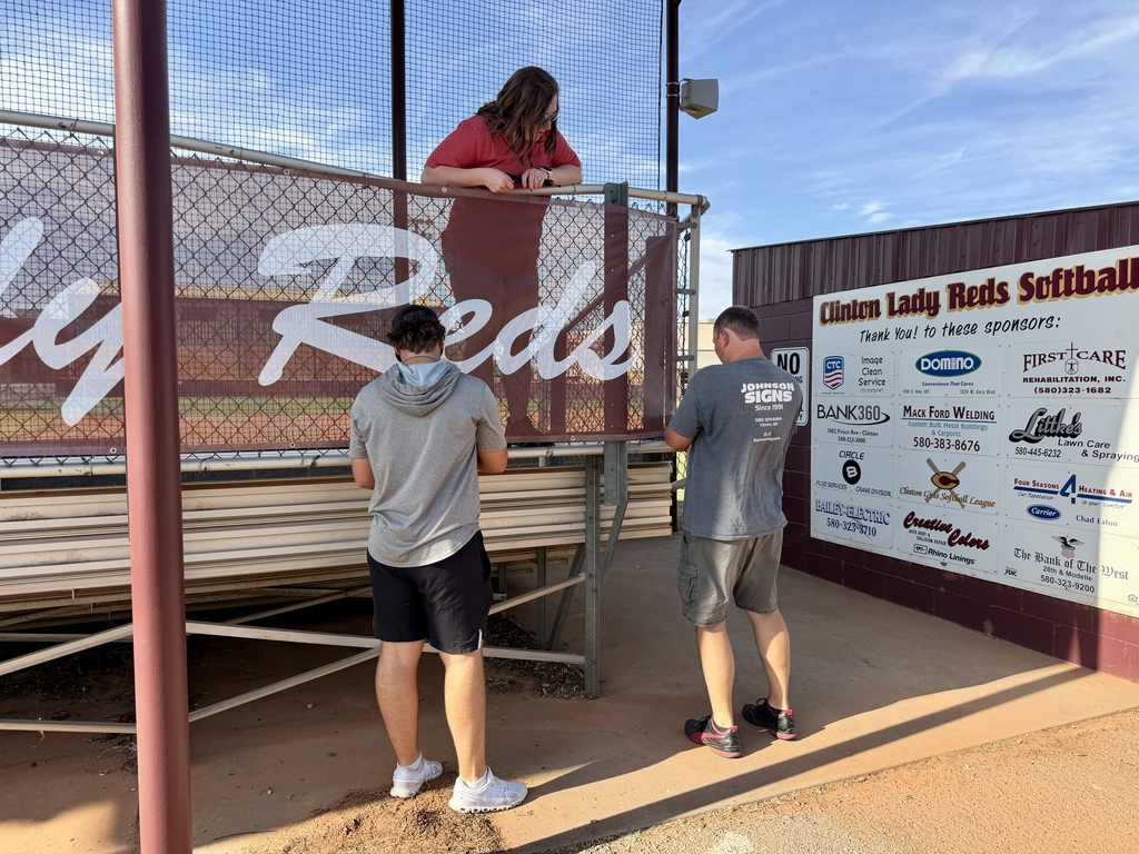 Workers installing mesh signage on the softball bleachers