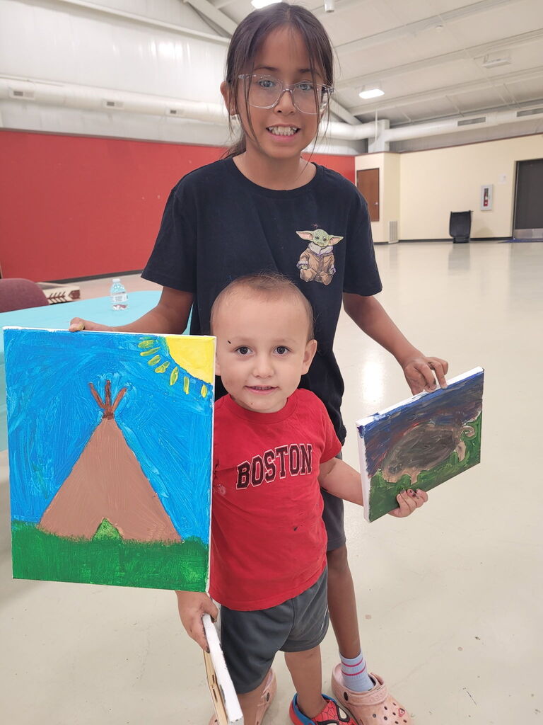 2 students looking at camera and holding a teepee painting