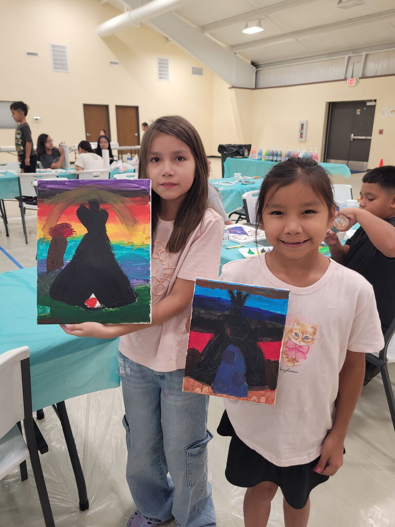 2 students holding colorful teepee paintings