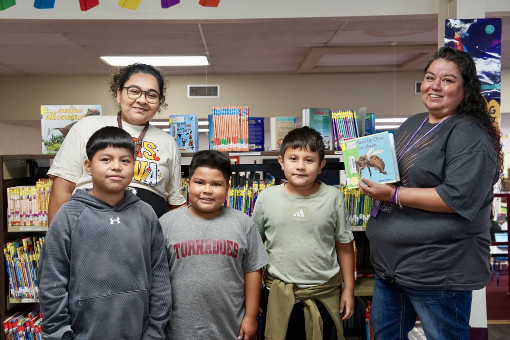 2 teachers and 3 students looking at a book in the library