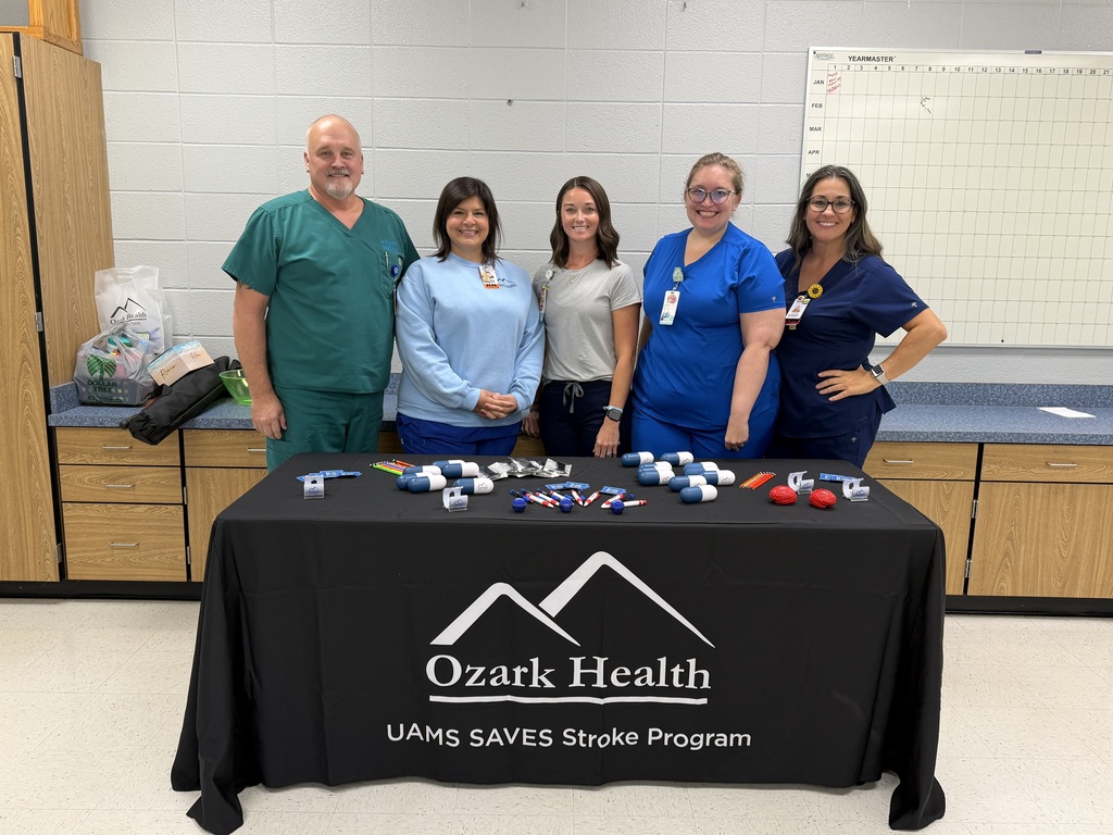 one male nurse and 4 female nurses standing behind a table