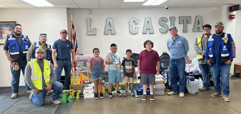 A photo of construction workers standing next to a pile of school supplies donated to La Casita Elementary school.