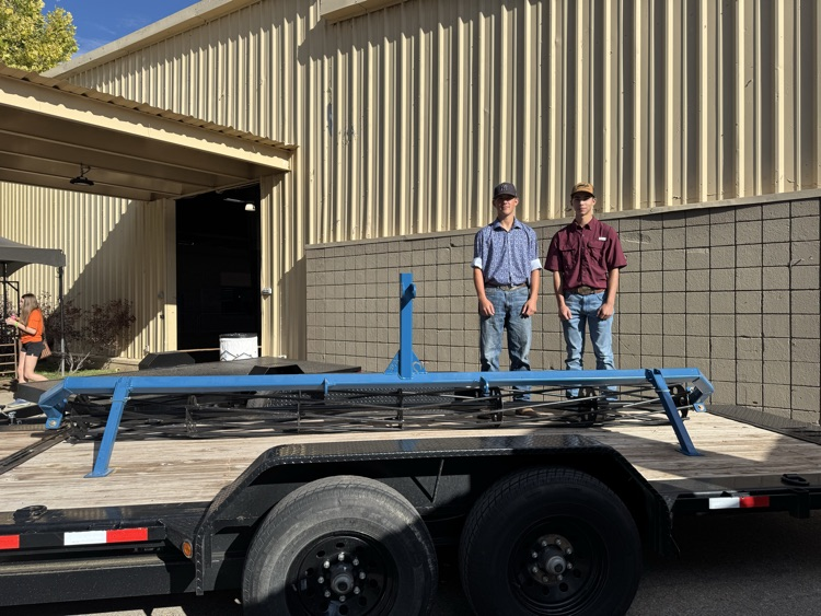 Two students stand by a trailer with a piece of equipment they created.
