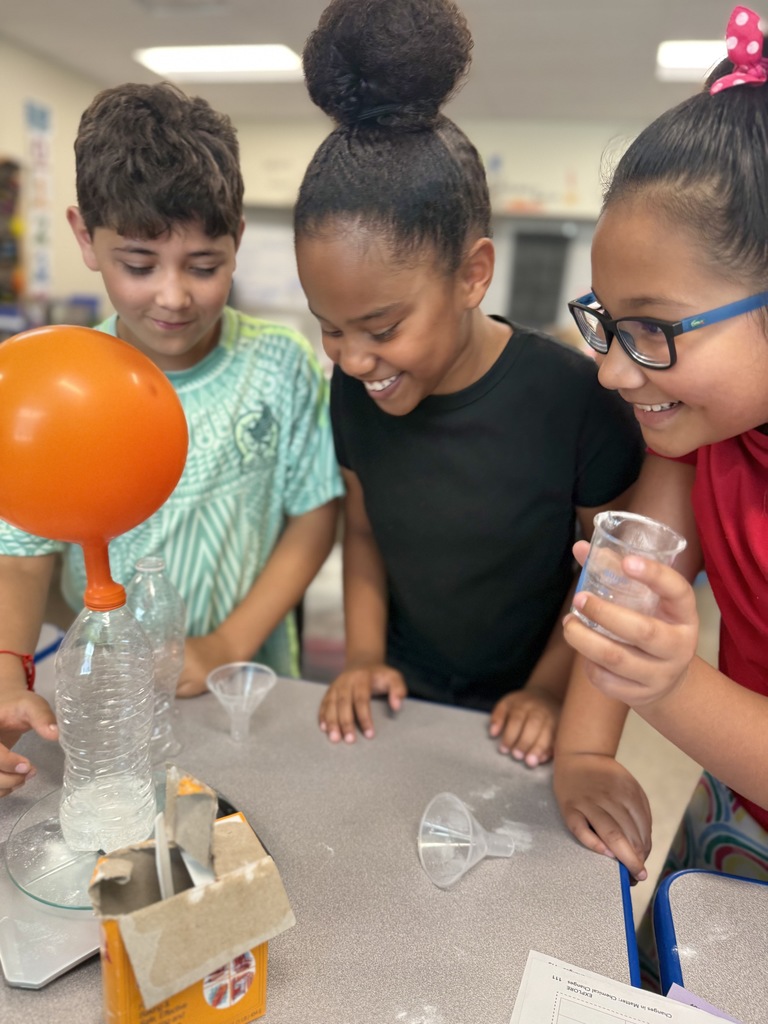 Three students smiling and looking a balloon being filled up with a bottle