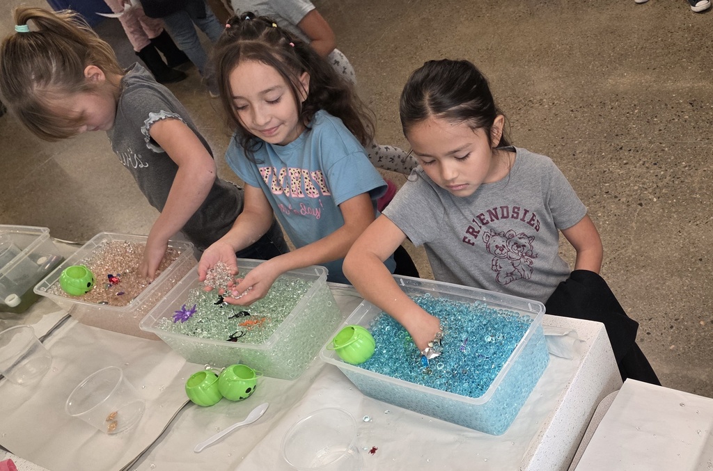 3 girl students with their hands inside sensory bins with water beads.