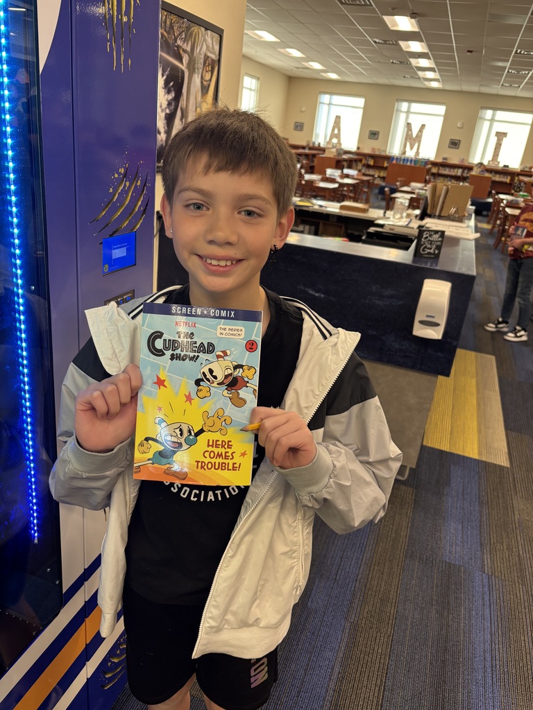 Male student, smiling and holding a book in front of book vending machine.