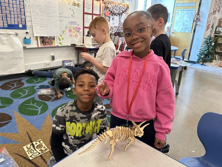 a pair students holding puzzle dinosaurs