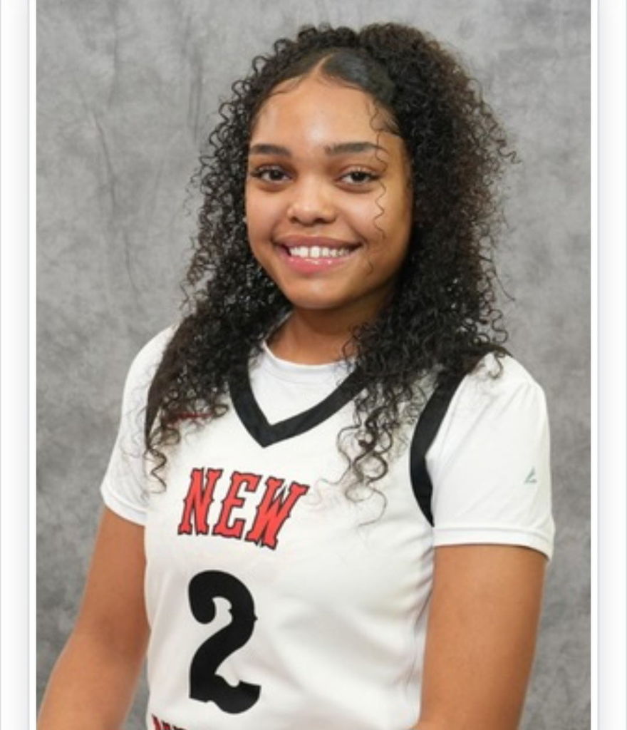 A girl with curly hair smiles, wearing a white jersey with black accents and the number 2.