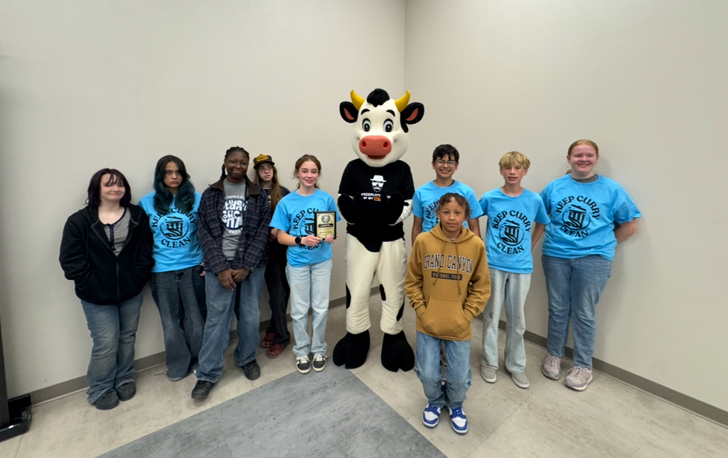 Group of teens in blue shirts and a mascot in a cow costume posing for a photo.