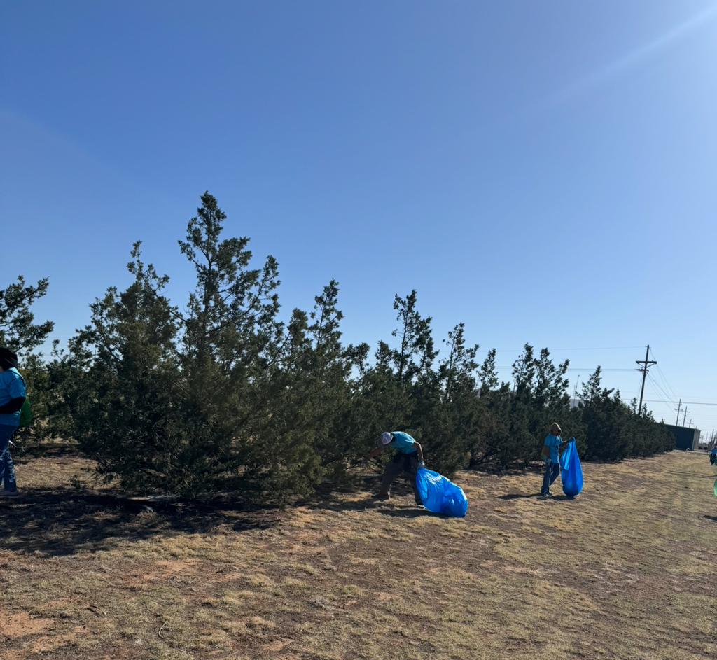 People in blue shirts and hats working in a field with trees and clear sky in the background.