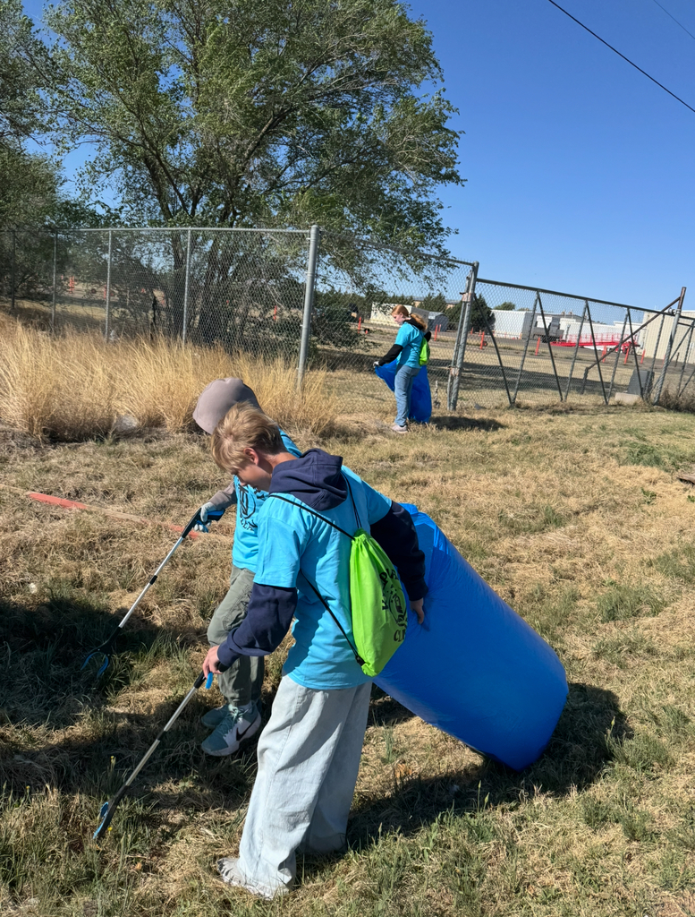 Two people are picking up trash in a field. One person has a blue backpack.
