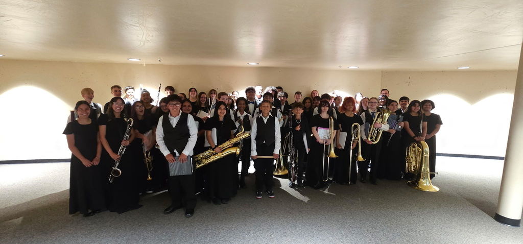 A group of musicians in black outfits, holding instruments, standing together in a bright room.