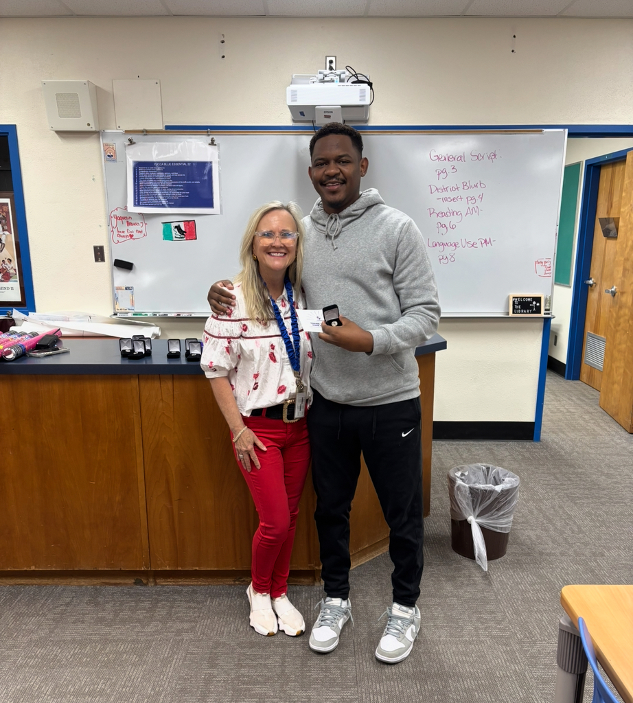A man and a woman standing together in a classroom. He holds a small item, possibly a medal.