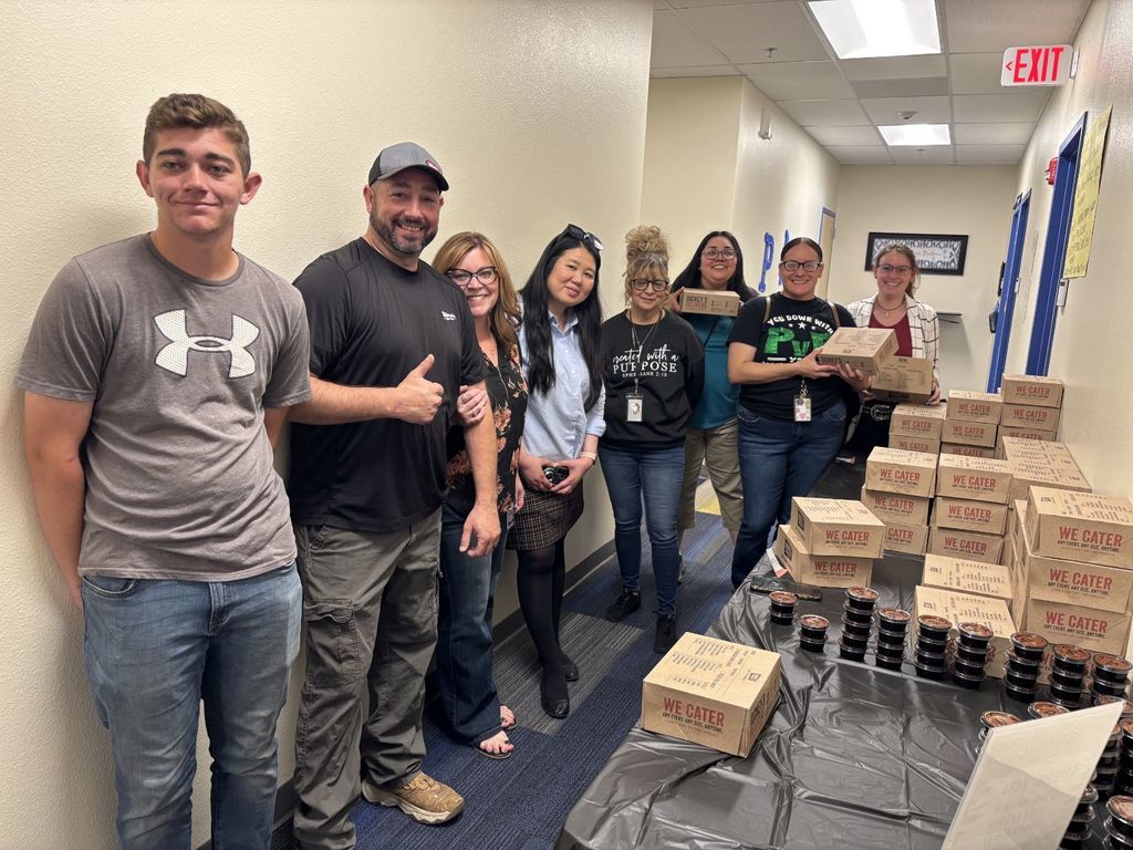 A group of people stand behind a table with boxes of food. A man gives a thumbs up.