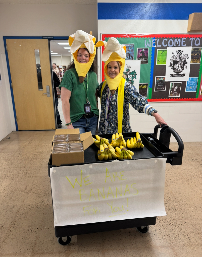 Two people in banana hats stand by a cart. The cart has bananas and a sign that says "We are bananas for you."