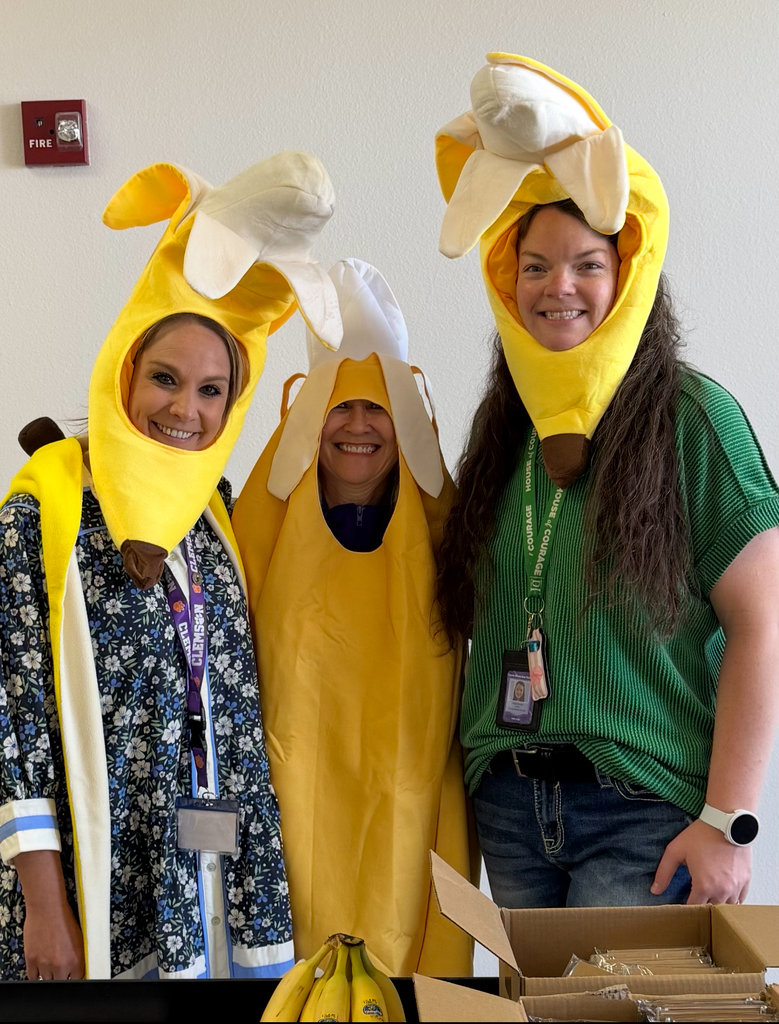 Three women in banana costumes smiling, one in green, one in yellow with a floral shirt, and one in blue.