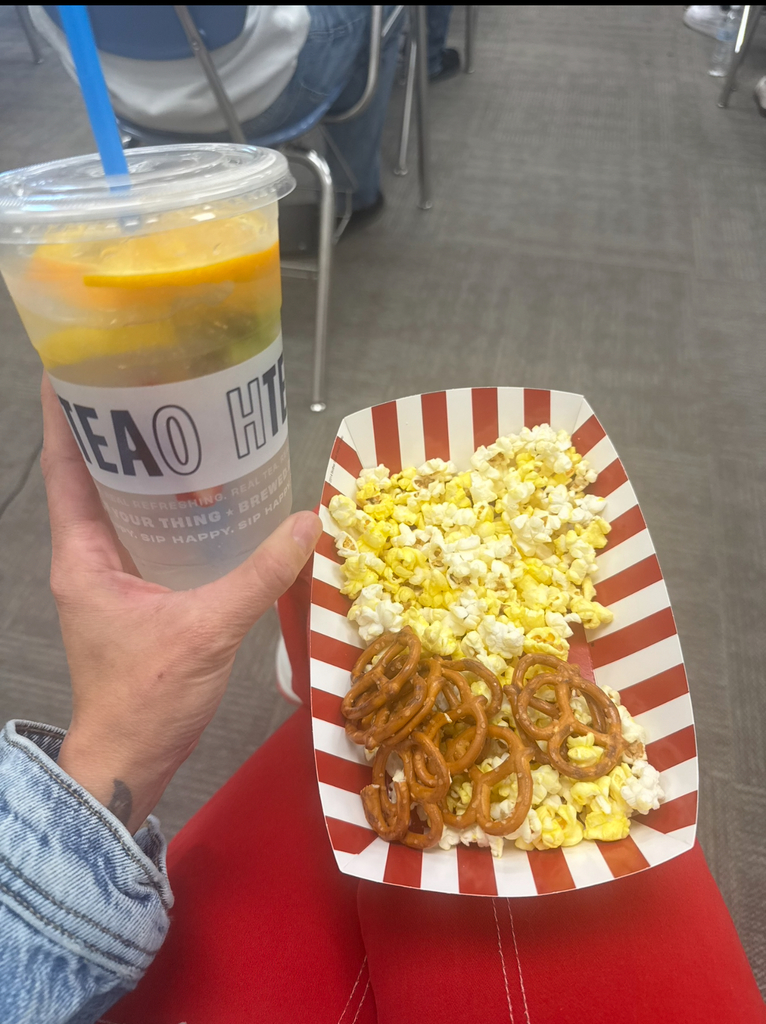 A hand holding a cup with a blue straw and a plate of popcorn with pretzels. 