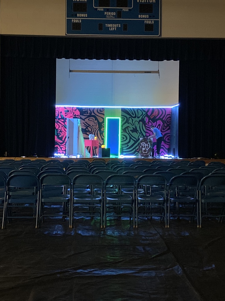 An empty auditorium with a stage featuring colorful backdrops and a person standing on the stage.