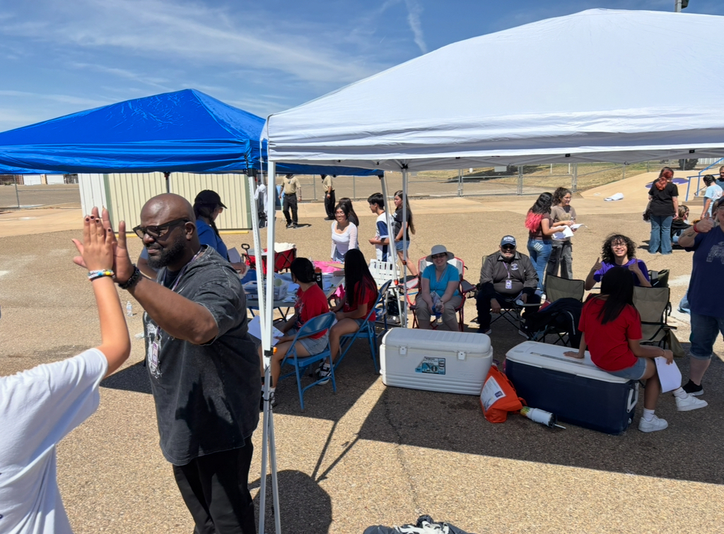 A group of people under two tents. One person giving another person a high-five. Coolers and chairs are present.