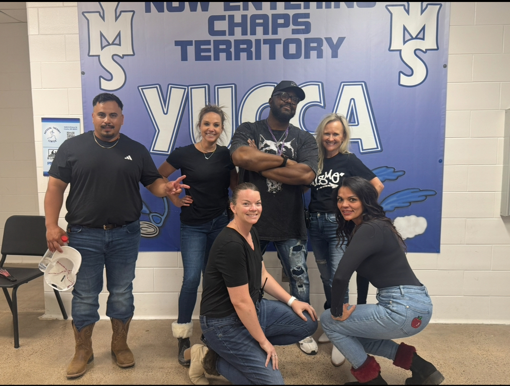 Six adults in casual clothing pose for a photo in front of a blue banner.