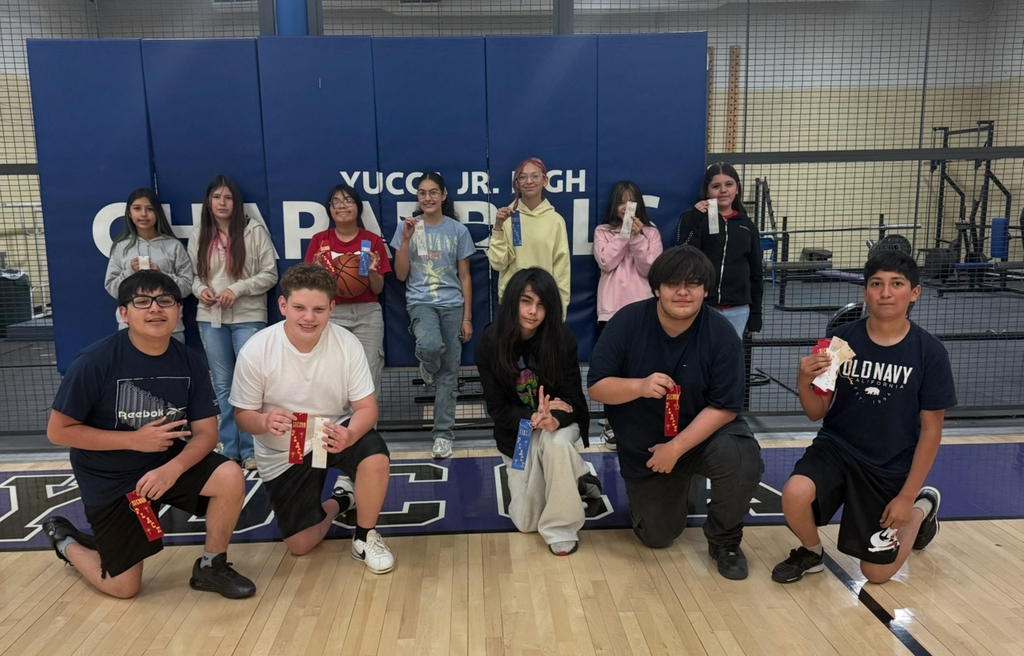A group of young people holding medals pose in front of a blue backdrop that reads "YUCCA JR. HIGH".