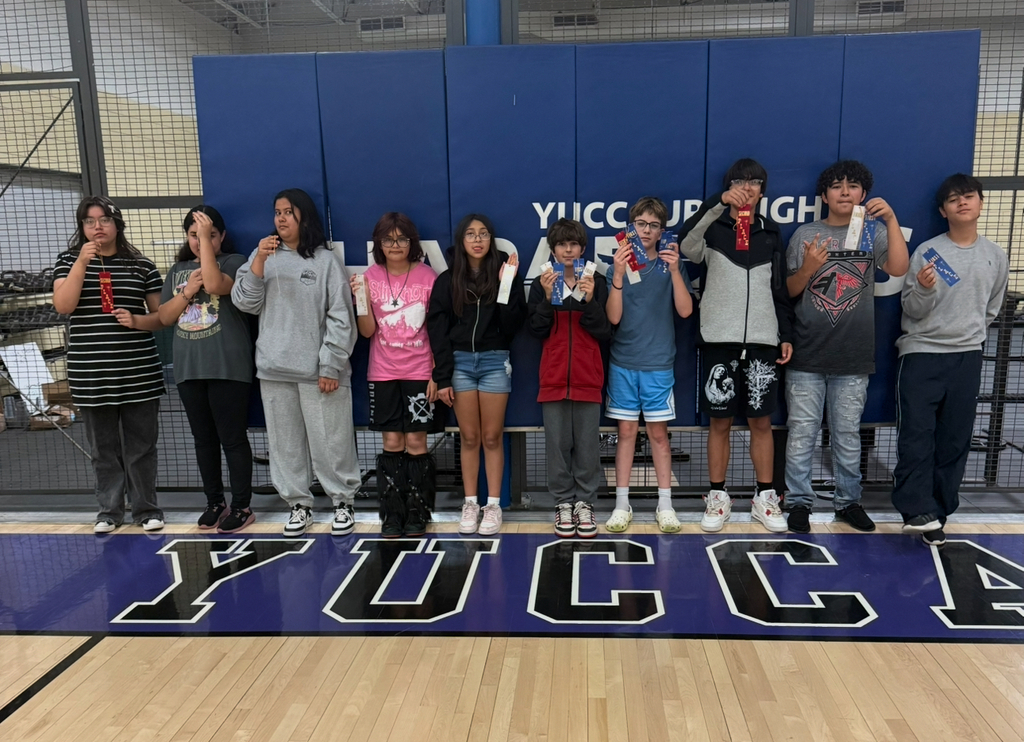 A group of students with medals pose for a photo in front of a blue wall with Yucca High text.
