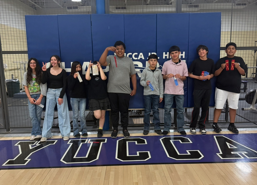 Group of students posing in front of a blue backdrop that says "Yucca High." They hold medals.