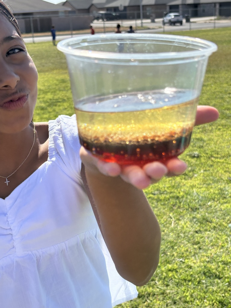 Girl holds a plastic cup of layered red and yellow liquid outdoors on a green lawn.