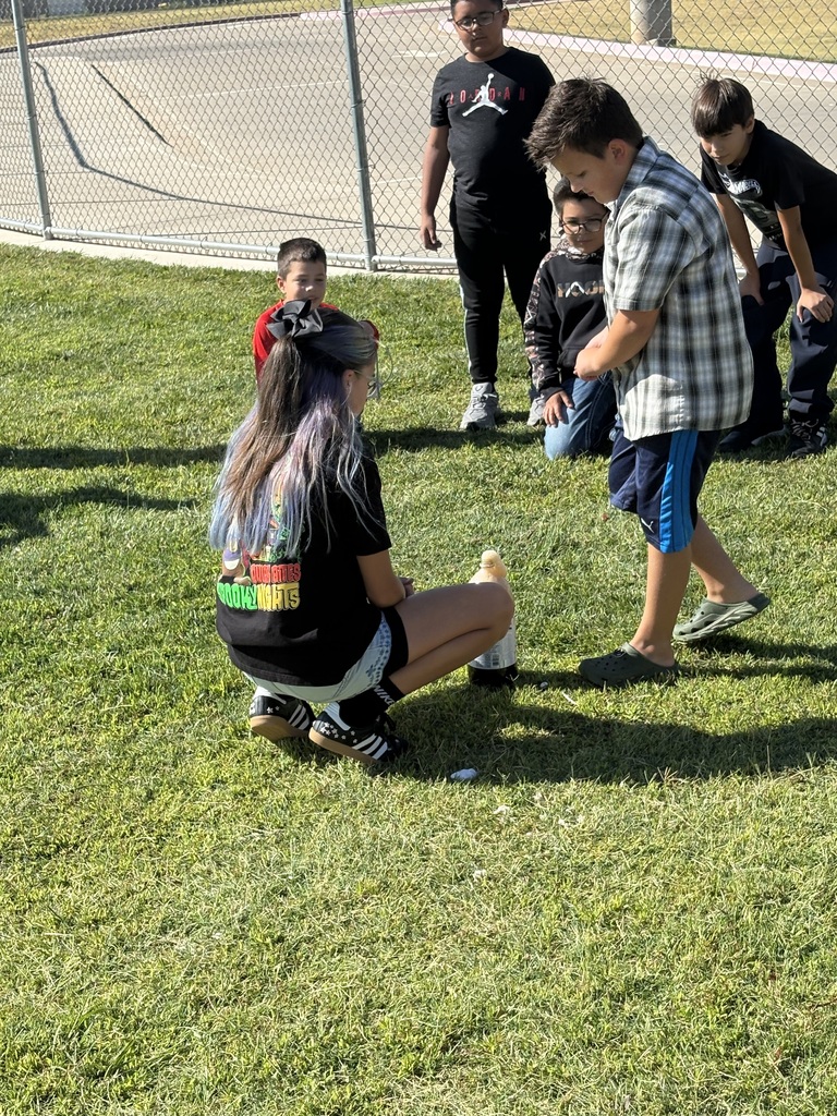 A group of children playing on a field. A woman crouches down, while a boy reaches for a soda bottle.