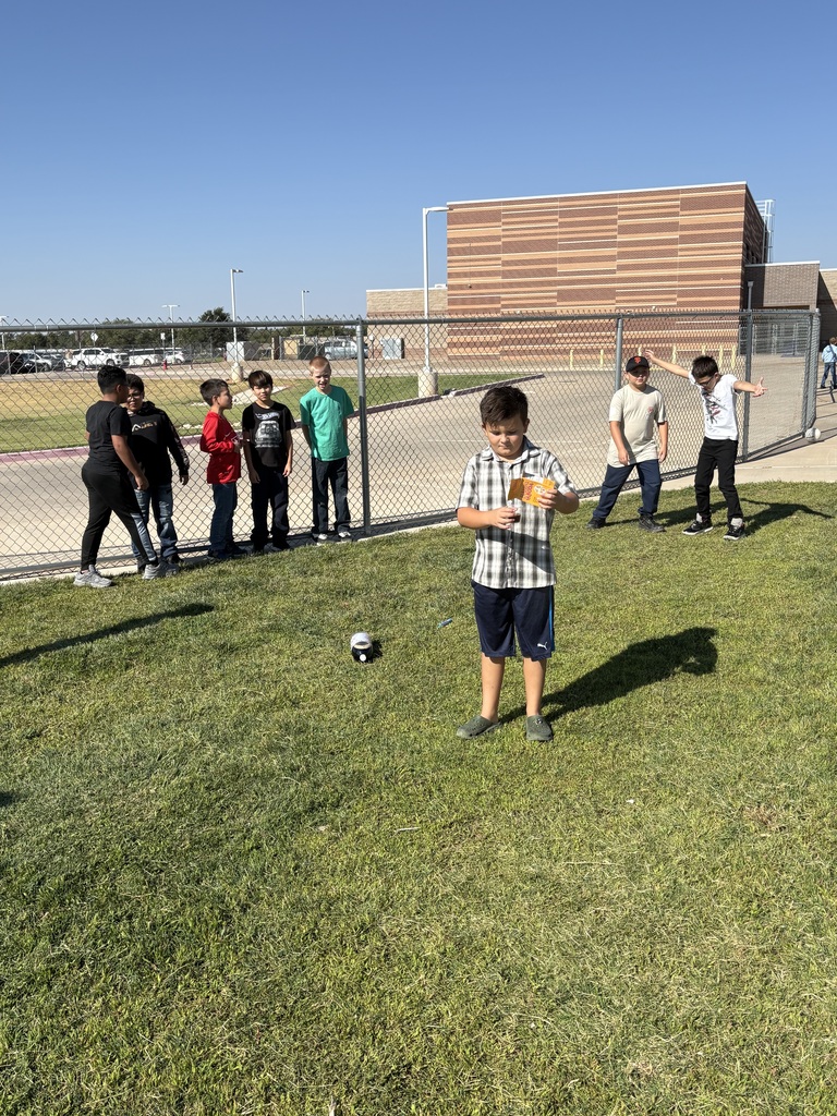 A group of kids are standing on a grassy field, playing with a soccer ball.