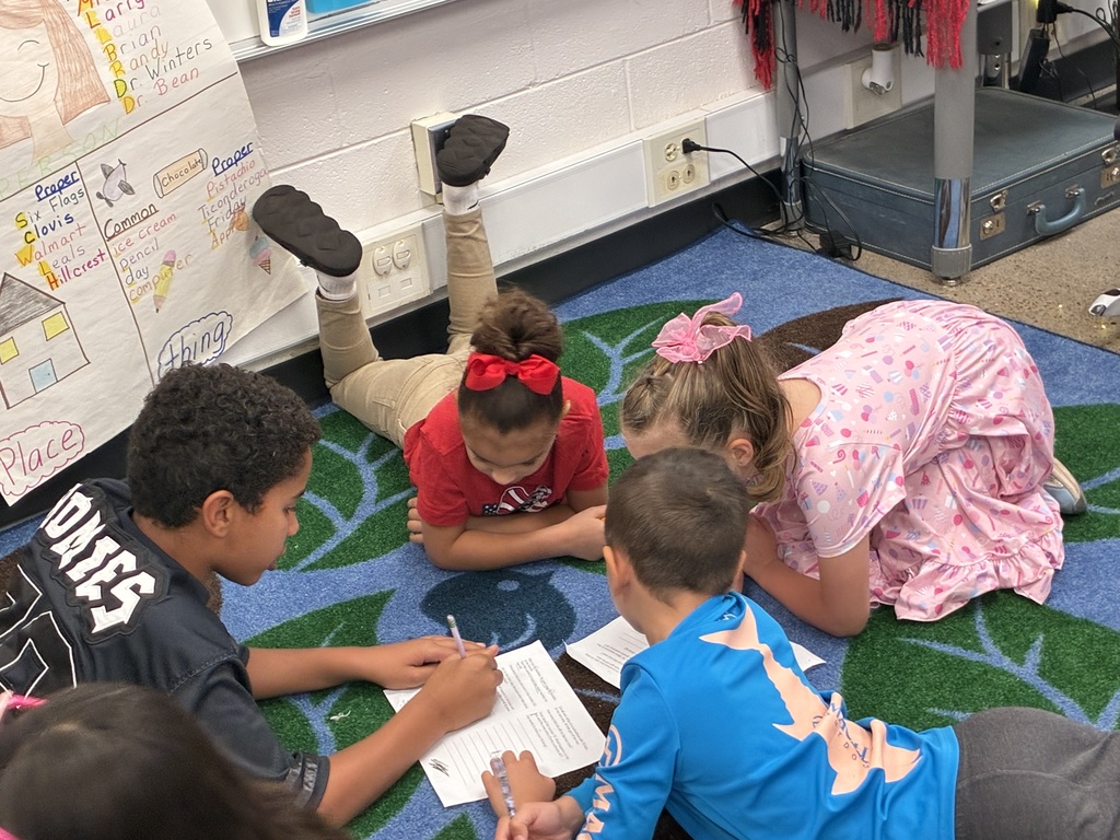 Five children on floor, some lying down, some sitting, one holding a pen, engaged in group activity.