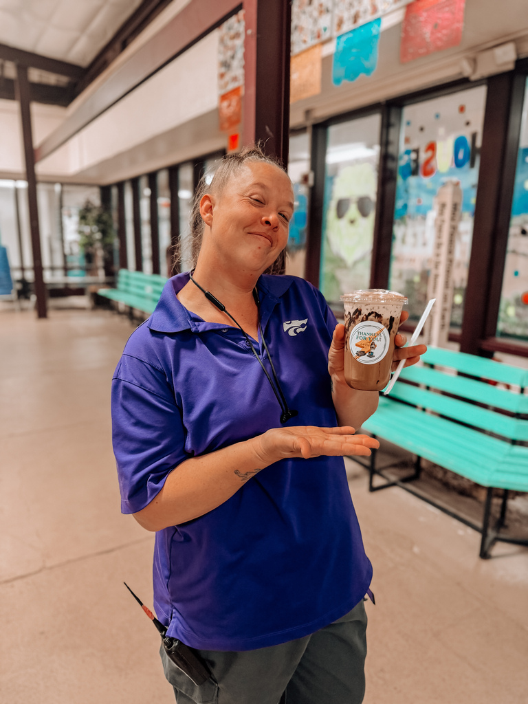 A person in a blue shirt holds a drink in a cafeteria with turquoise benches.