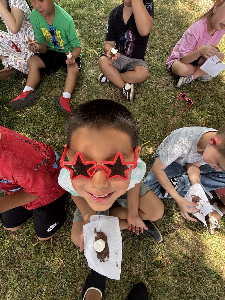 Kids sitting on the grass, holding ice cream and other food items, smiling and looking at the camera.