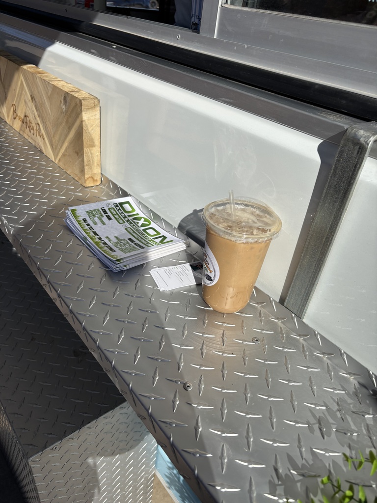 A metal counter has a cup of coffee, a pamphlet, and a wooden block on it.