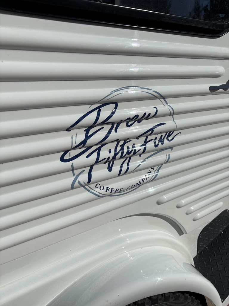 A white vehicle displays a logo that reads "Brown Fifty Five Coffee" in blue cursive font on a curved surface.