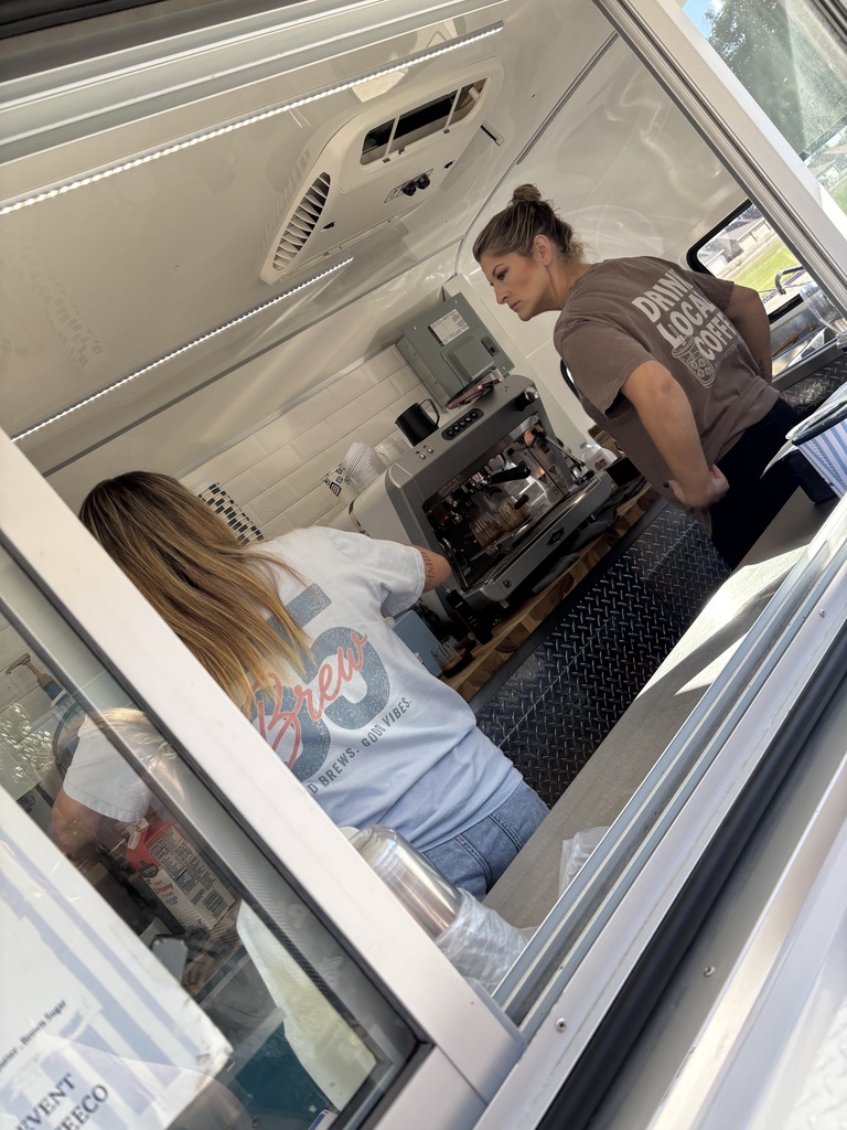 Two people inside a food truck. One with blonde hair and a white shirt. The other with a brown shirt.