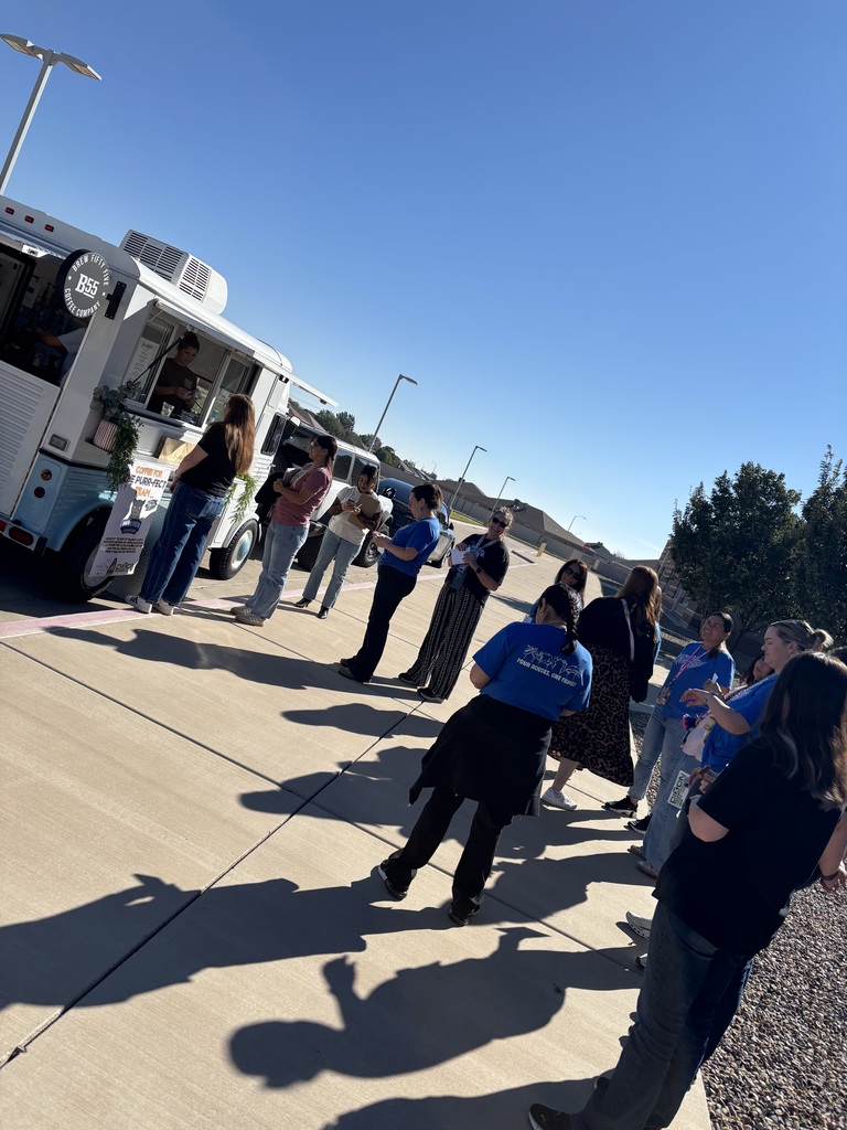 Group of people stand in line at a food truck under a blue sky, near trees.