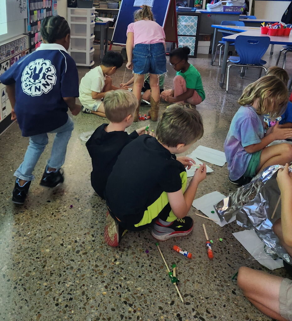 Group of children, some sitting on floor and others standing, engaged in an art project.